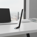 TP-Link Archer TX35U Plus Wi-Fi 6 USB adapter on an office desk with a blurred workspace background.
